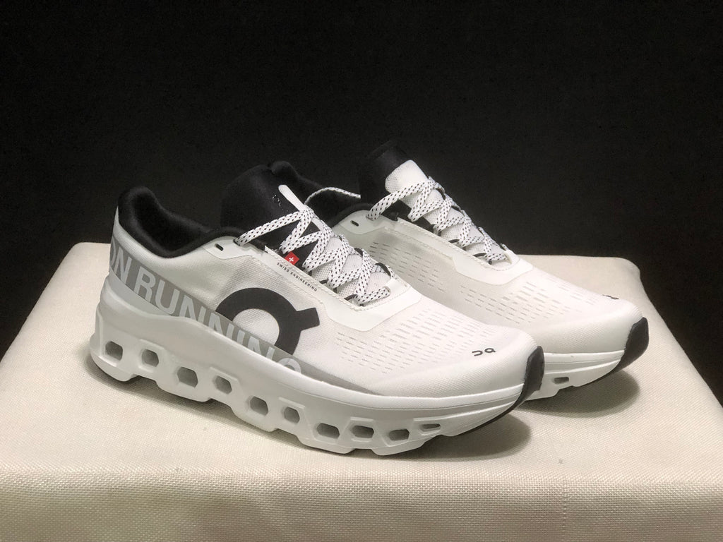 Front three-quarter view highlighting the white uppers, black toe accents, patterned laces, and open sole details.