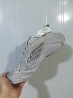 Underside and side view of the beige New Balance 9090 sneaker showing the textured outsole and layered upper construction.