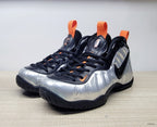 Pair of silver, black, and orange Nike Air Foamposite Pro sneakers viewed from the front and side