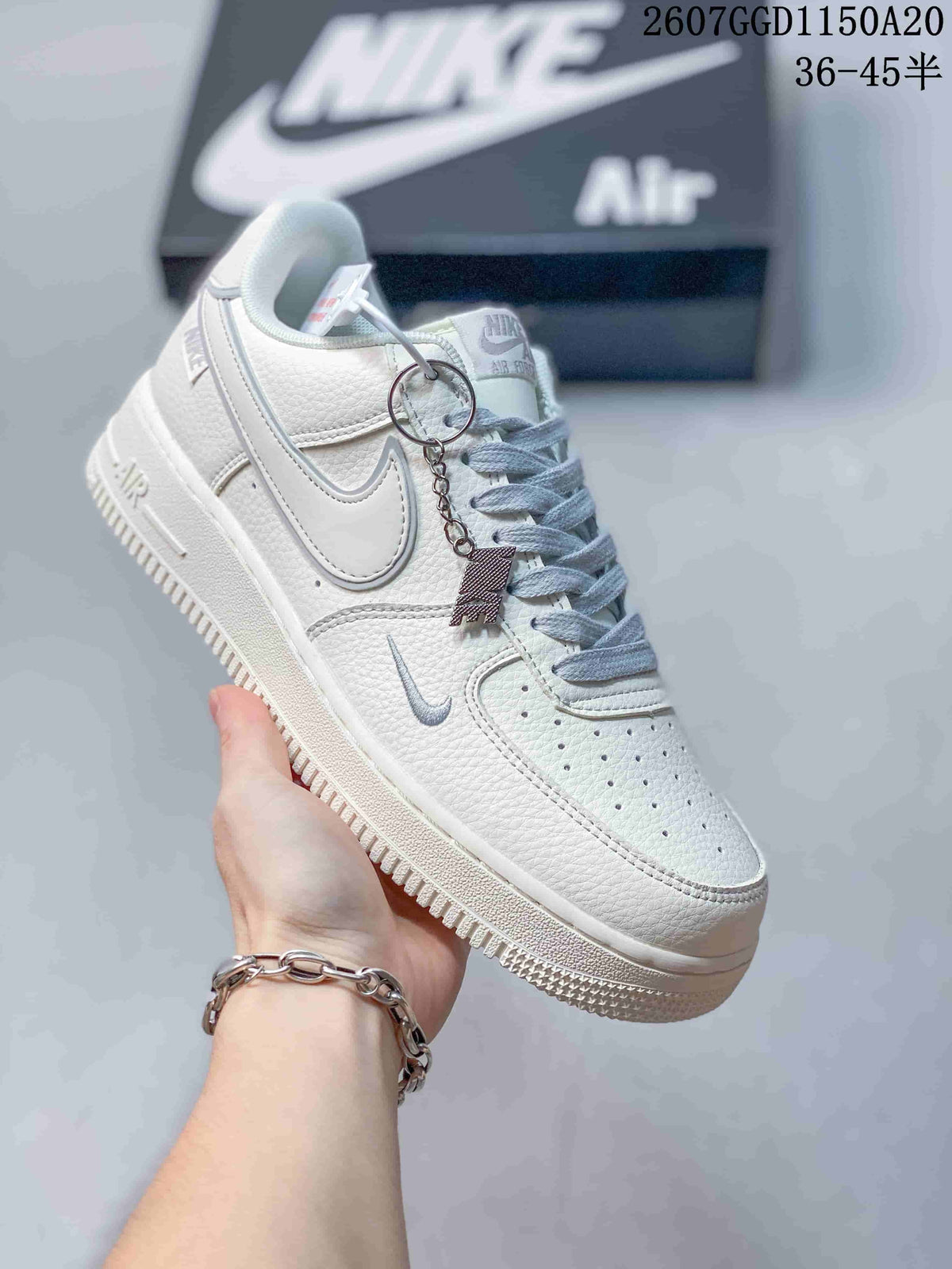 Close-up of a white Nike low-top sneaker with light gray Swoosh branding, pale gray laces, and a perforated toe box.