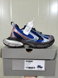 Royal blue, silver, black, grey, and pink low-top sneaker displayed on its box; the box label shows “REFLECTIVE/NW,” “ROYAL/GREY,” and size “C 37.”