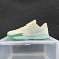 Side view of a cream Nike basketball sneaker with a light blue Swoosh, green accents and a pale aqua sole.