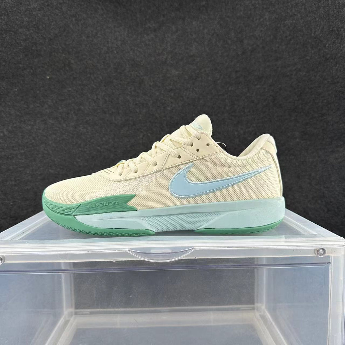 Side view of a cream Nike basketball sneaker with a light blue Swoosh, green accents and a pale aqua sole.