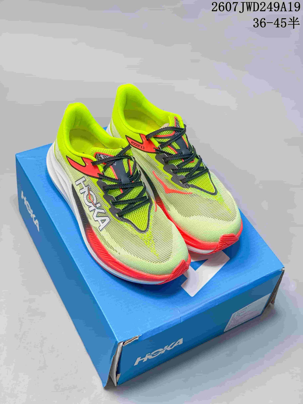 Pair of bright green and coral Hoka running shoes displayed on a blue Hoka shoebox.
