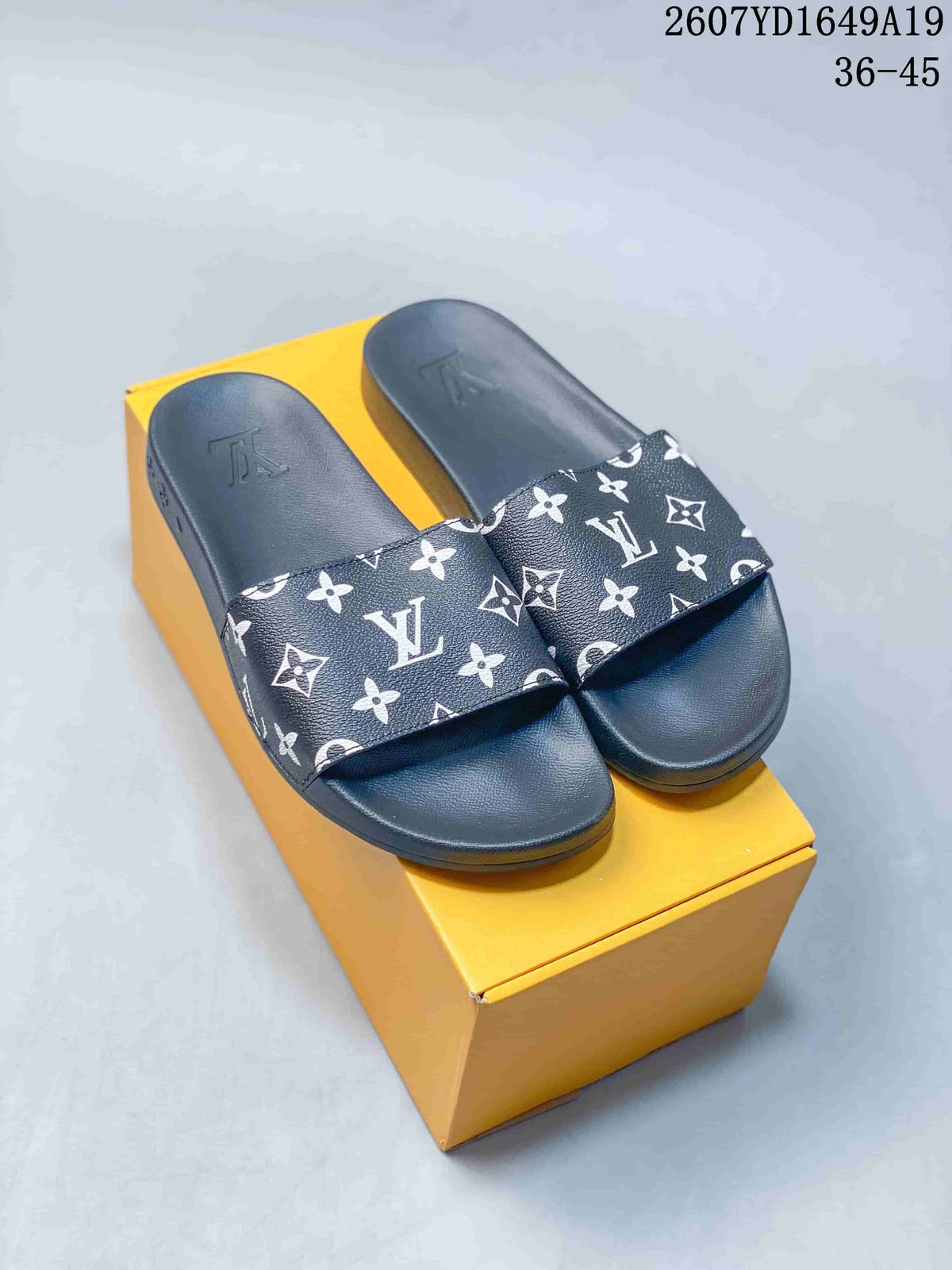 Pair of black-and-white monogram slide sandals displayed on a yellow box.