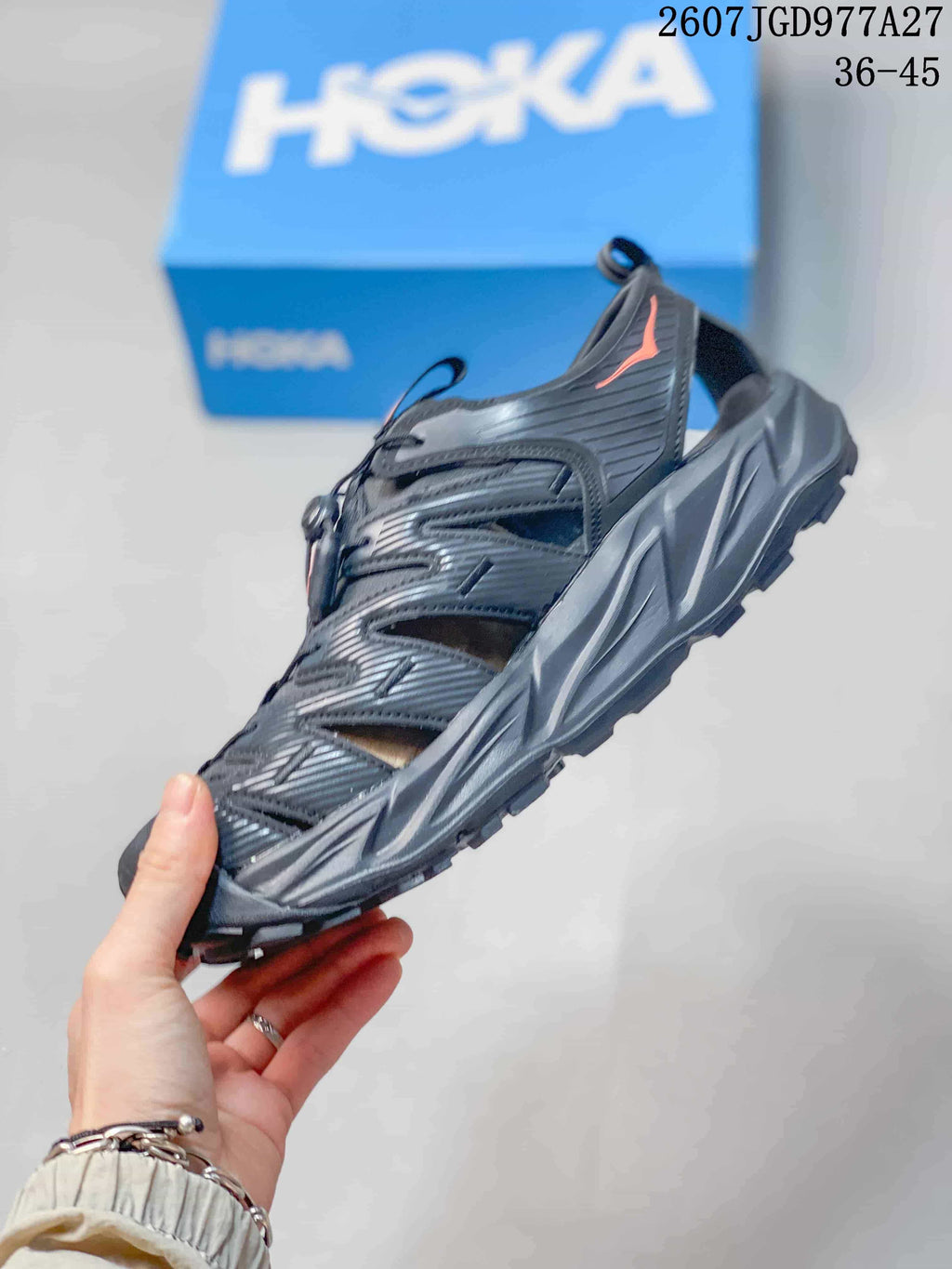 Side profile of a black and charcoal HOKA Hopara OG sandal showing the open-sided upper, toggle lacing and sculpted sole.