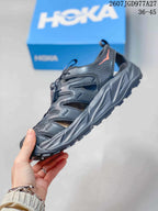 Side profile of a black and charcoal HOKA Hopara OG sandal showing the open-sided upper, toggle lacing and sculpted sole.