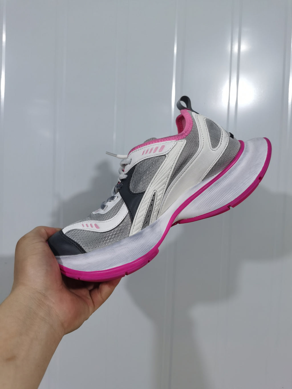 Side view of a grey, white and pink Balenciaga Circuit sneaker held against a light background.
