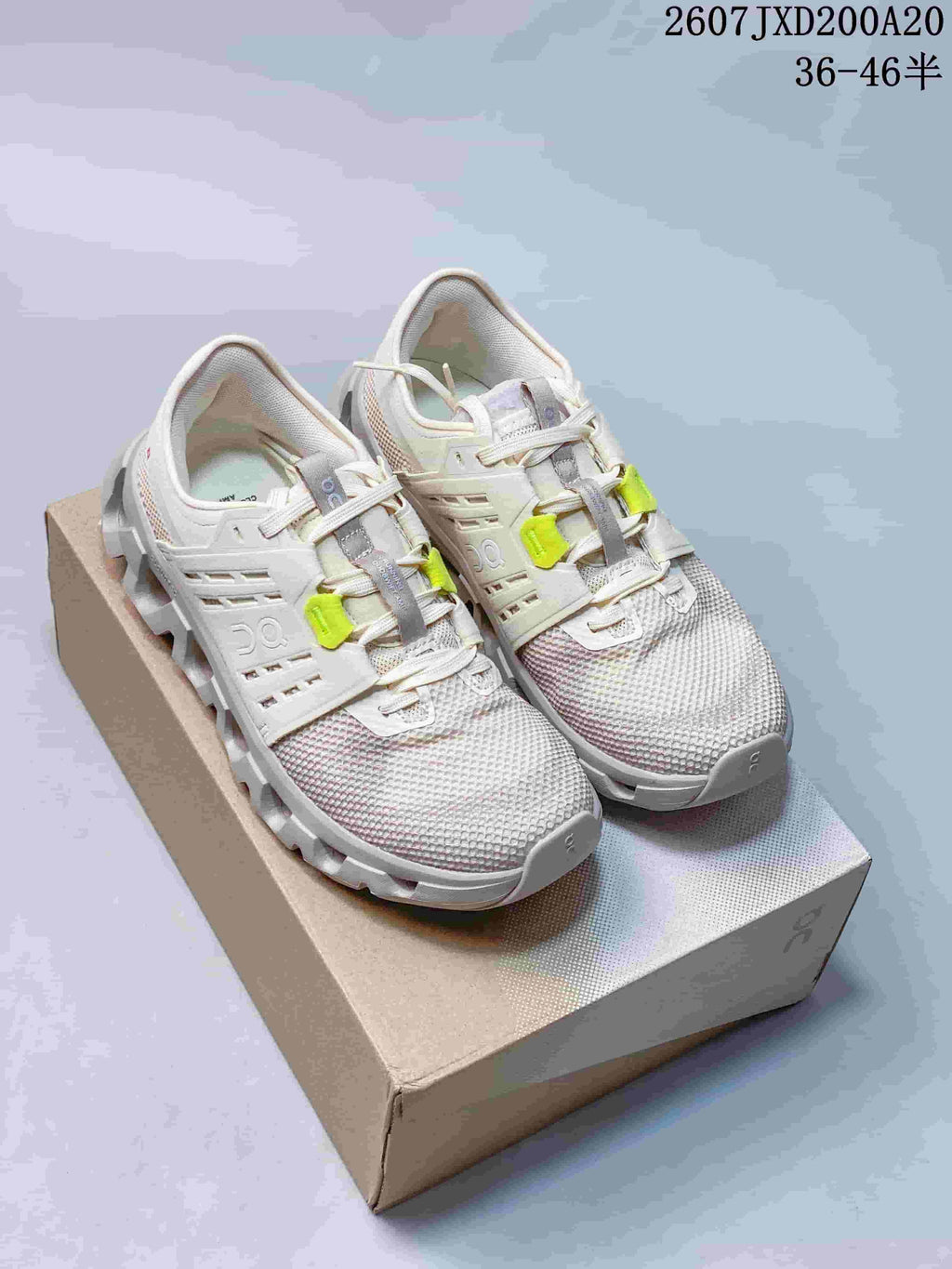 Pair of white and light gray On sneakers with neon yellow lace details displayed on a shoebox.
