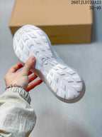 Underside view of a white sneaker showing the patterned rubber outsole and central outsole emblem.