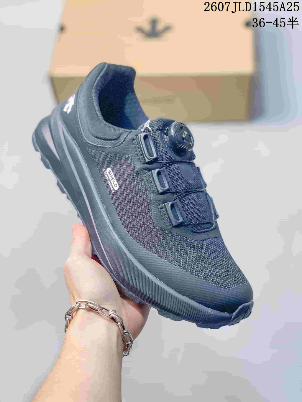 Three-quarter view of the black DESCENTE SHIELD sneaker showing the mesh upper, side branding, dial closure, and low-top profile.