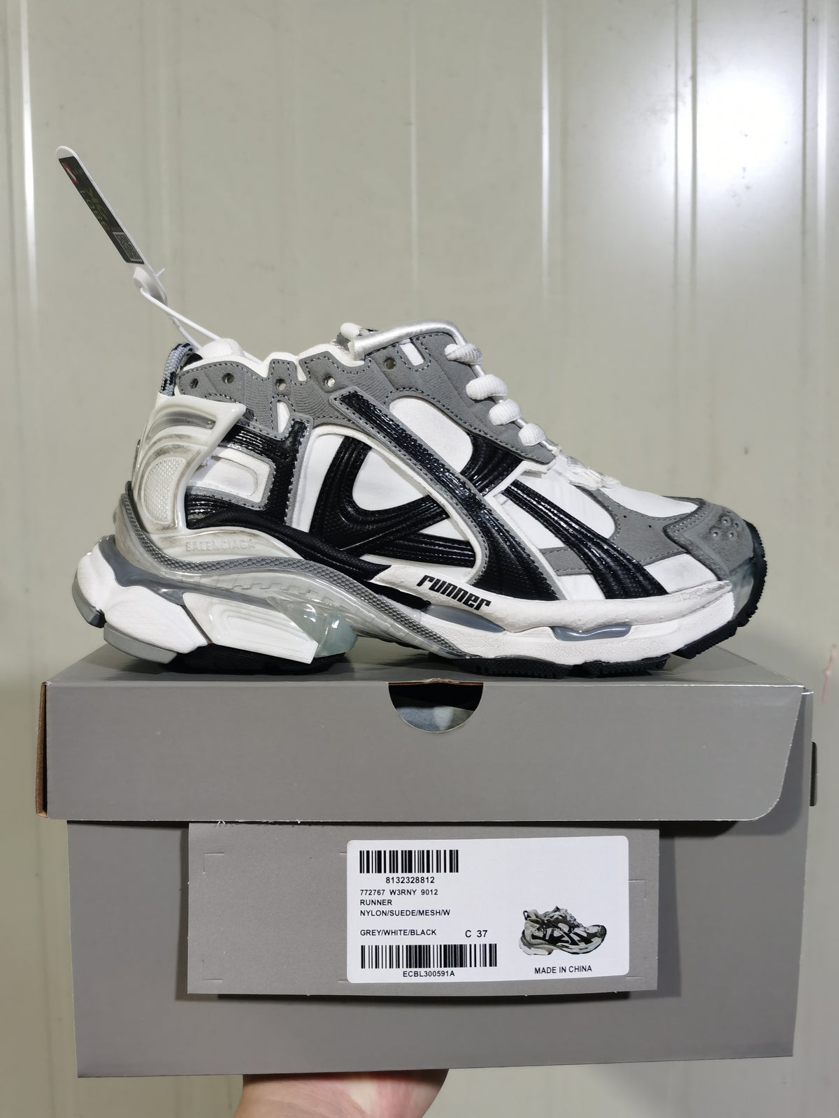 Side view of the Puma 9012 Runner sneaker displayed on its shoebox; the box label shows style code 772767 W3RNY 9012, color Grey/White/Black, and sample size C 37.