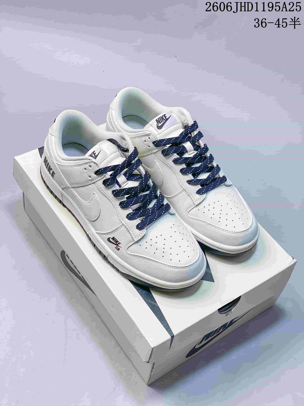 Pair of white low-top sneakers with navy patterned laces, perforated toe boxes, and contrast Swooshes.