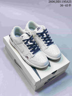 Pair of white low-top sneakers with navy patterned laces, perforated toe boxes, and contrast Swooshes.