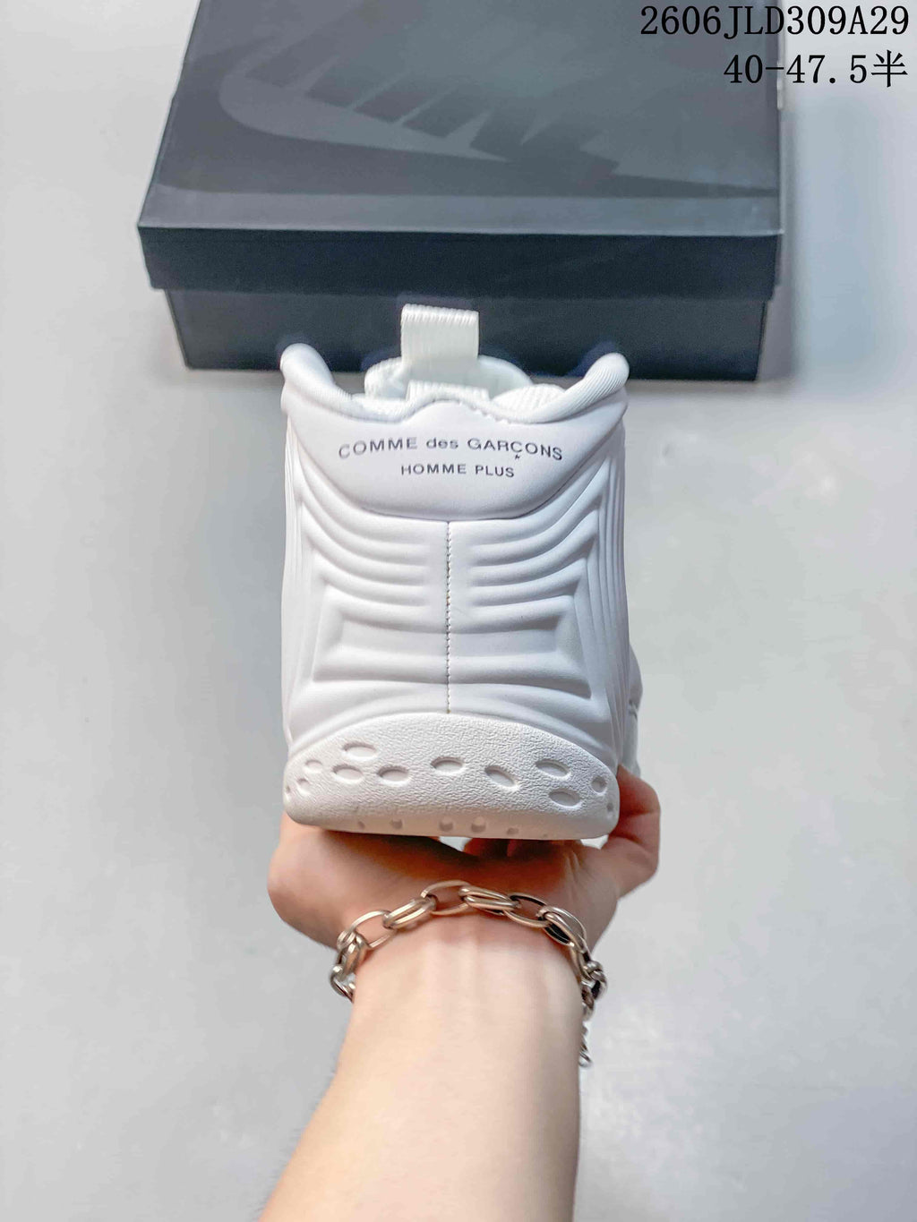 Rear view of a white sneaker with Comme des Garçons Homme Plus text on the heel.