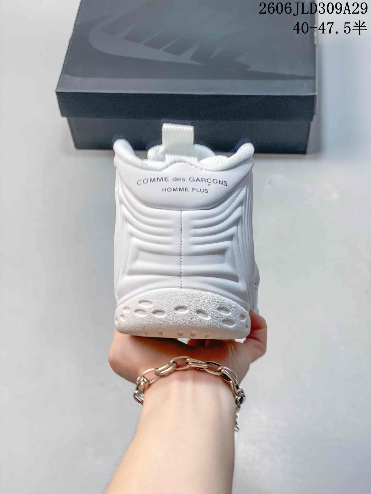 Rear view of a white sneaker with Comme des Garçons Homme Plus text on the heel.