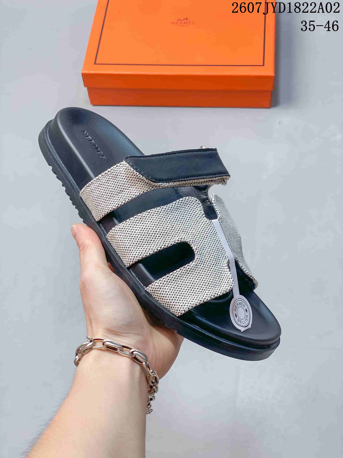 Close view of a dark Hermès Kazimir slide sandal with a light patterned upper.
