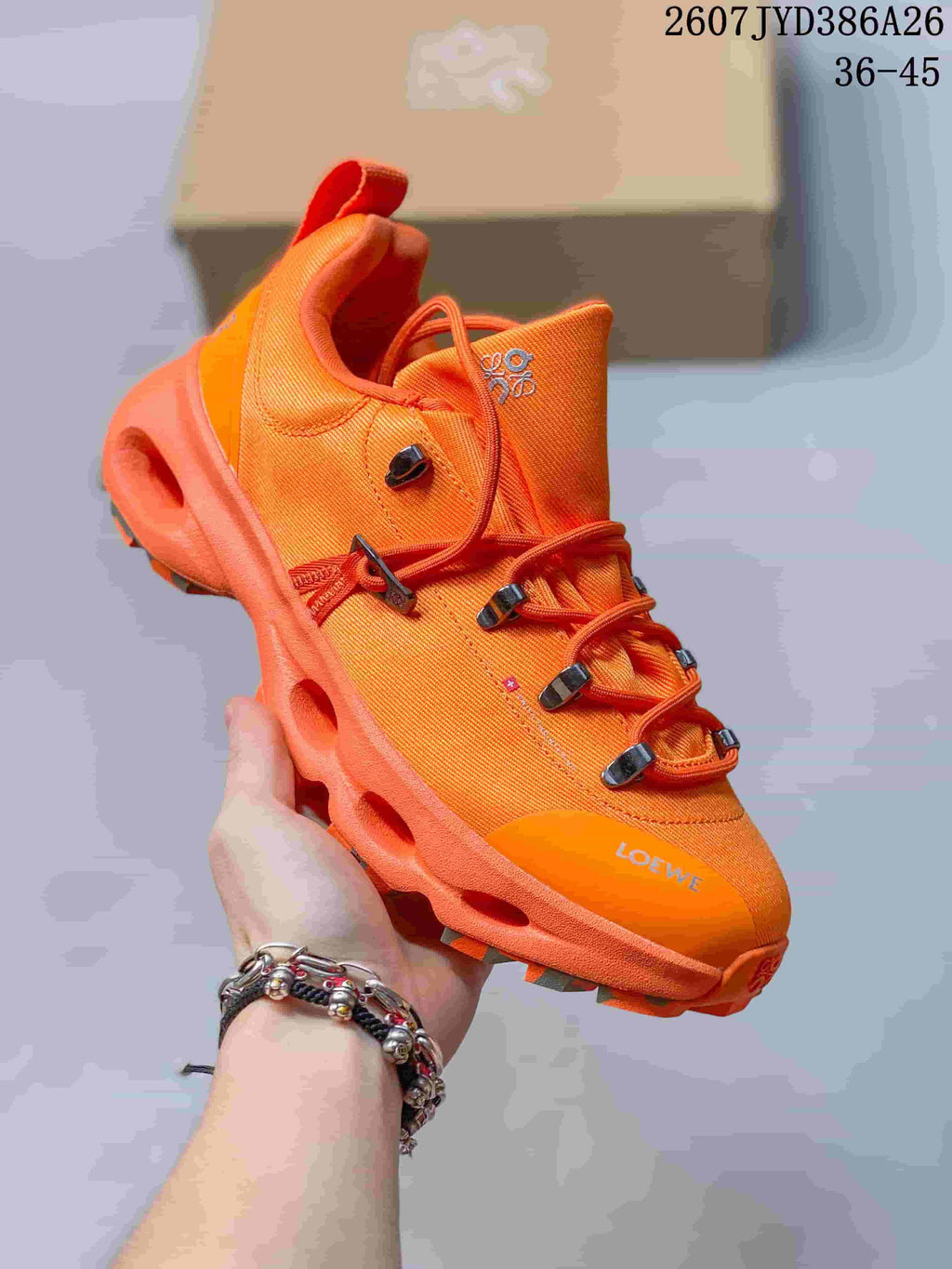 Angled close-up of an orange On LOEWE series sneaker showing the textured upper, lace hardware, heel pull tab, and sculpted sole.