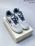 Pair of white, navy, and gray low-top sneakers displayed on a shoebox, showing dark laces and yellow tongue accents.