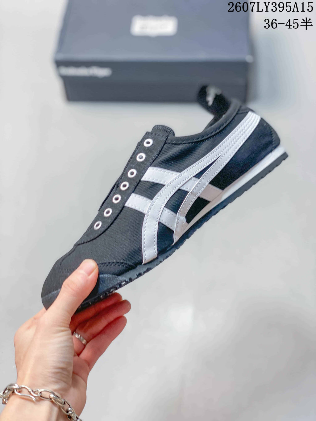 Side view of the black sneaker showing white Onitsuka Tiger stripes, metal eyelets, a padded collar, and a low-profile sole.