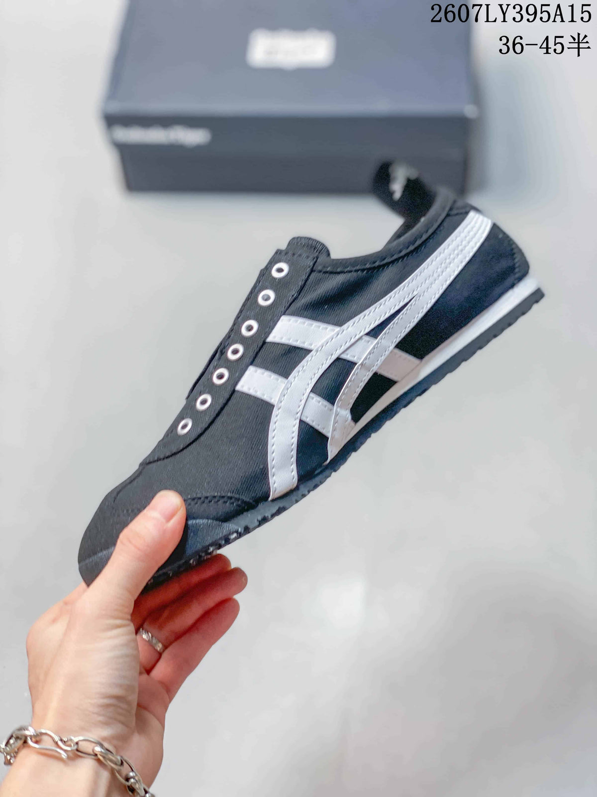 Side view of the black sneaker showing white Onitsuka Tiger stripes, metal eyelets, a padded collar, and a low-profile sole.