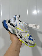 Angled close-up of the white Nike 9074 Runner 2 sneaker showing layered panels, mesh-style sections and blue and yellow accents.
