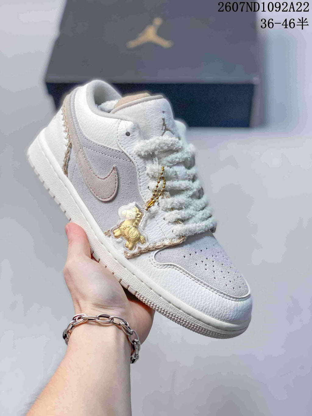 White and light gray low-top Jordan sneaker with textured laces and a teddy bear charm.