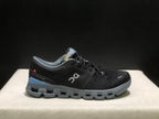 Side view of one black On Cloud X4 shoe showing the logo, gray sole, blue heel accent, and visible Swiss Engineering text.