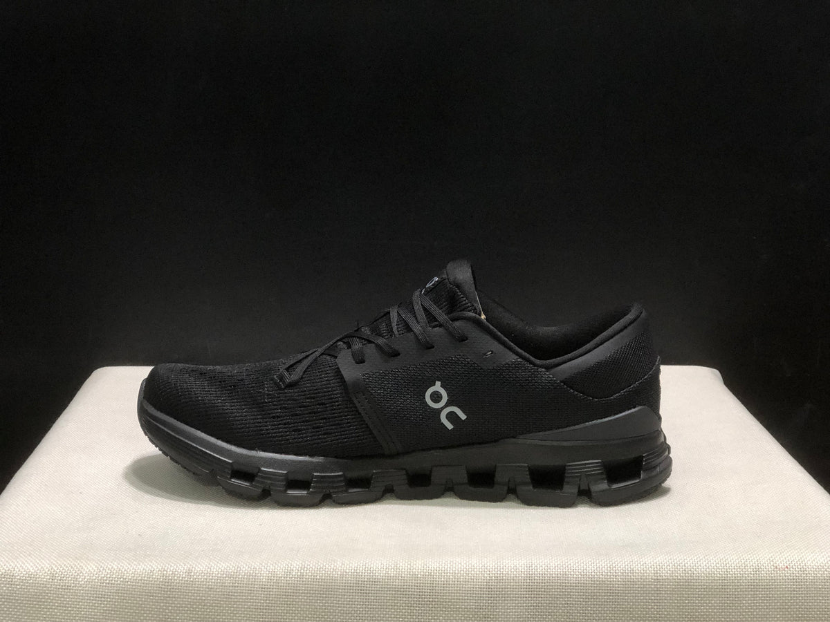 Side profile of a black On Cloud X4 shoe showing the low-top shape and segmented outsole.