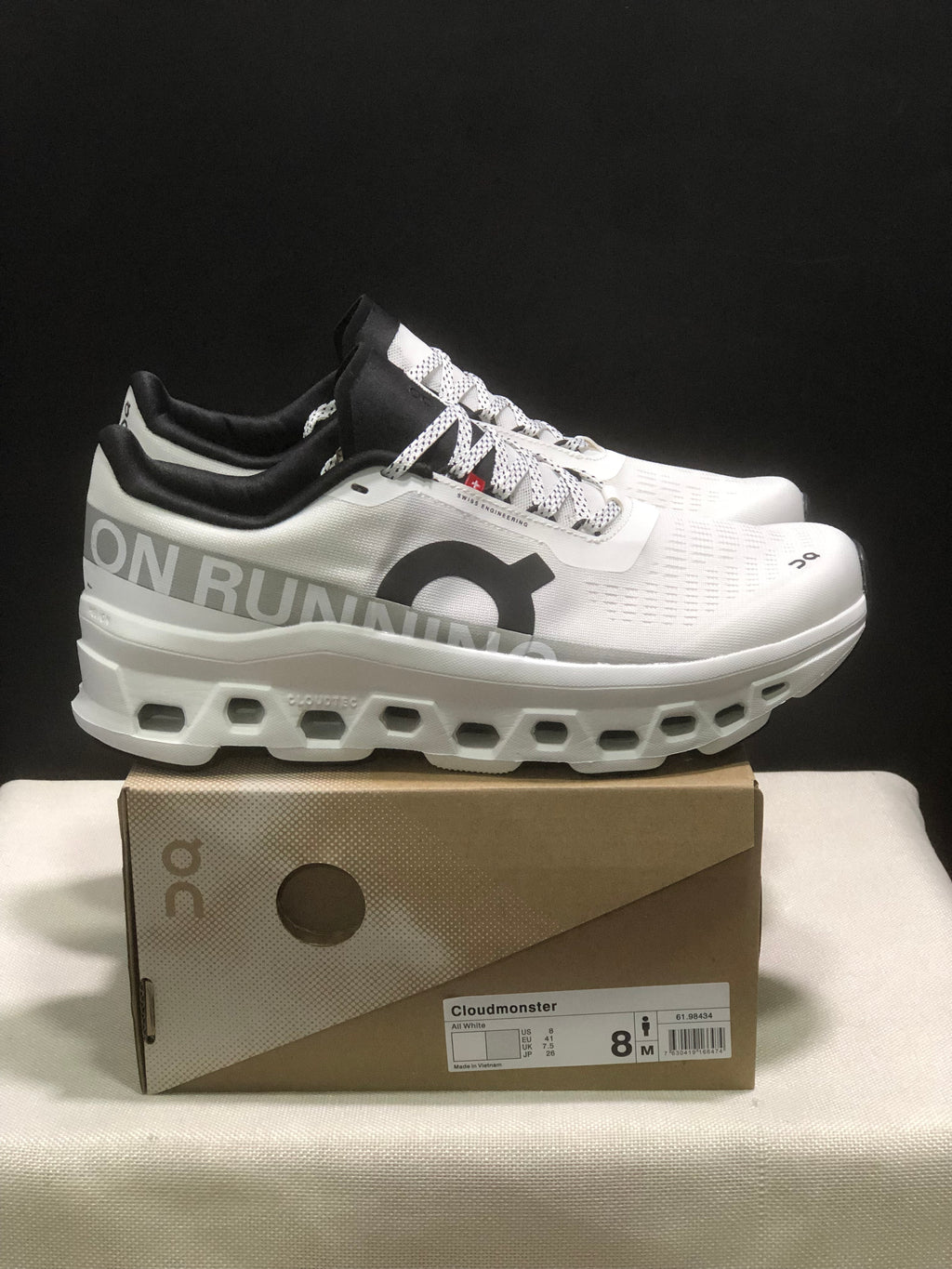 Side view of white On Cloudmonster sneakers showing the black collar, patterned laces, side branding, and sculpted sole.