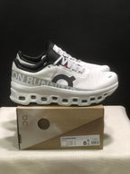 Side view of white On Cloudmonster sneakers showing the black collar, patterned laces, side branding, and sculpted sole.
