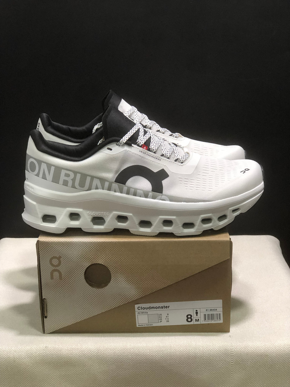 Side view of white On Cloudmonster sneakers showing the black collar, patterned laces, side branding, and sculpted sole.