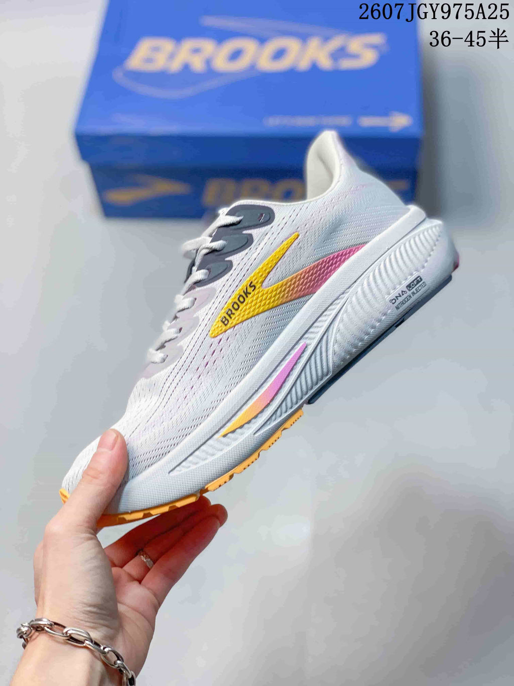 Side profile of a white Brooks running sneaker with a yellow-to-pink side logo and layered sole.