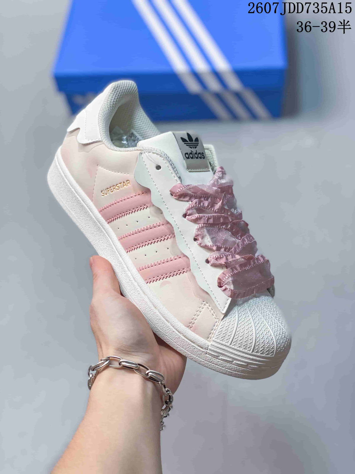 Angled side view showing the Superstar branding, pink side stripes, shell toe, and ruffled laces.