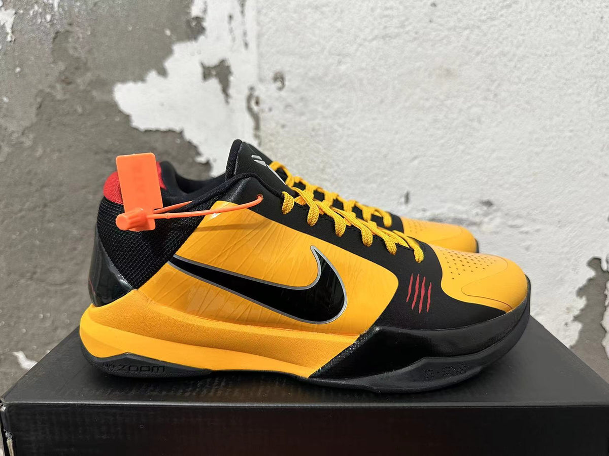 Side view of a black and yellow Nike Kobe basketball shoe with a Swoosh and red accents