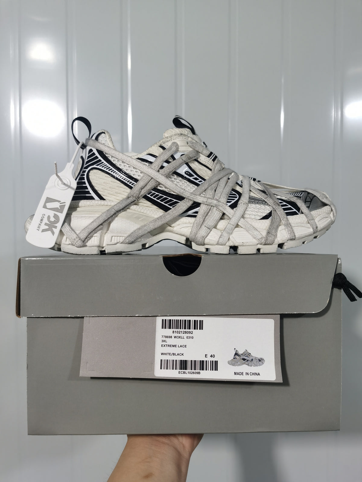 White and black sneaker displayed on a gray shoebox; the visible label shows style 0310, color WHITE/BLACK, and size E 40.