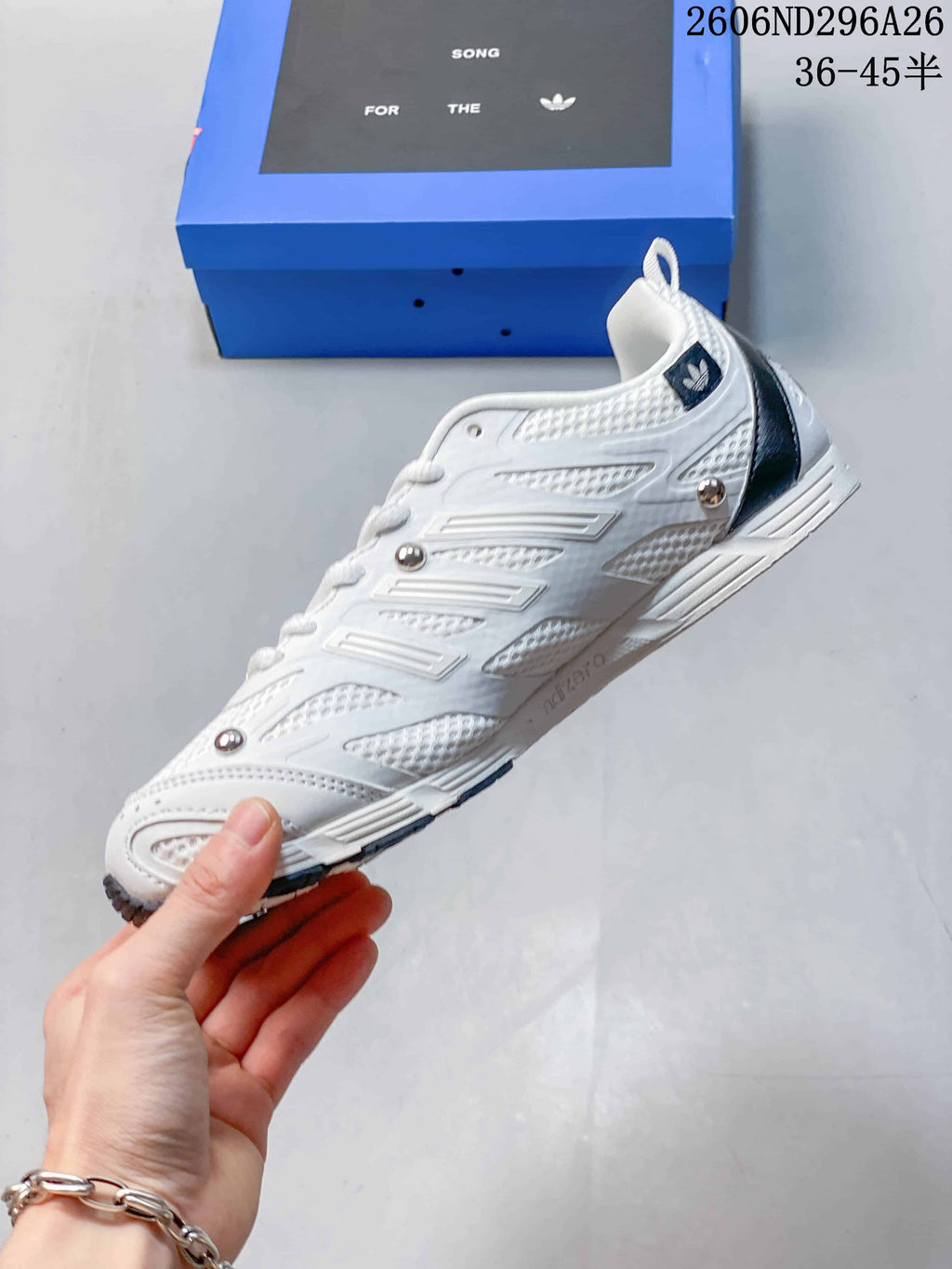 Side view of the white sneaker showing textured panels, dark accents and metallic-tone round details.