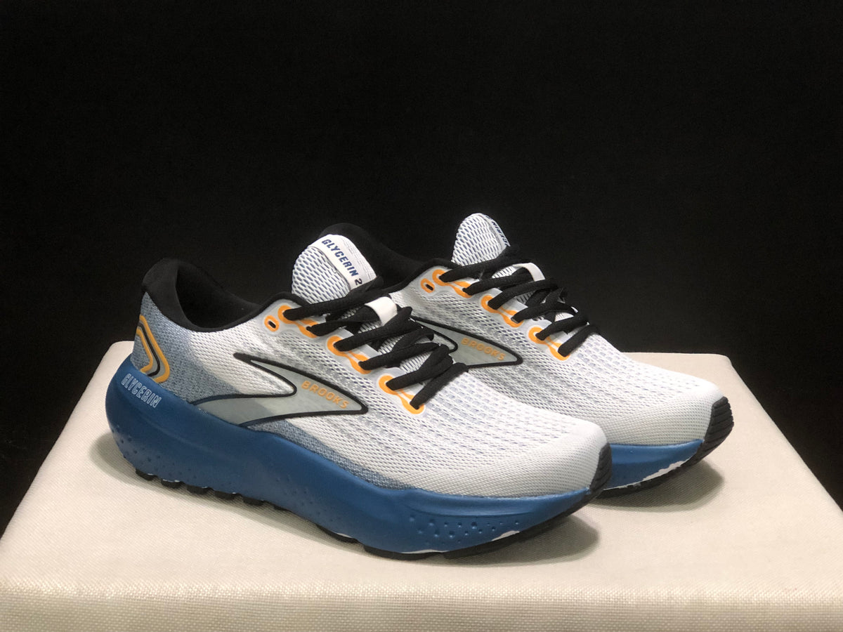 Front three-quarter product view showing the white uppers, black laces, blue midsoles, and orange accents.