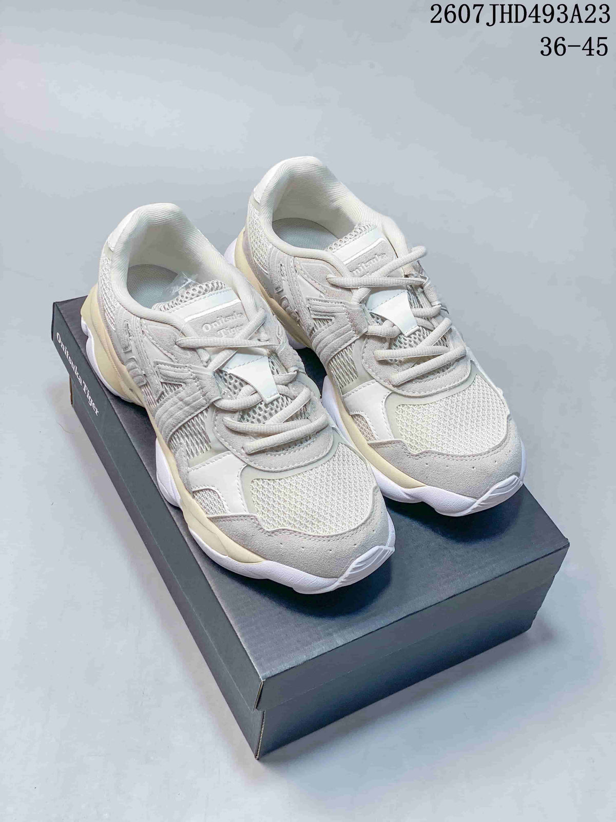 Pair of white and gray Onitsuka Tiger TIGRUN sneakers displayed on a shoebox, showing the layered upper and sculpted sole.