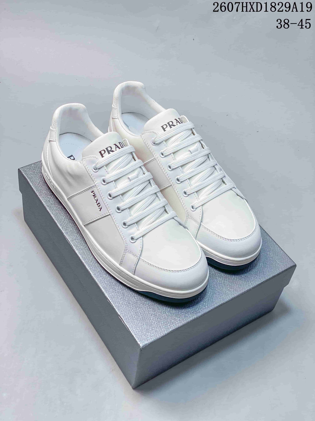 Pair of white Prada Downtown low-top sneakers displayed on a shoebox, with style code 2607HXD1829A19 and size range 38–45 visible above.