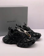 Three-quarter view of black sneakers with pull tabs, padded collars, and a Balenciaga-branded box in the background.