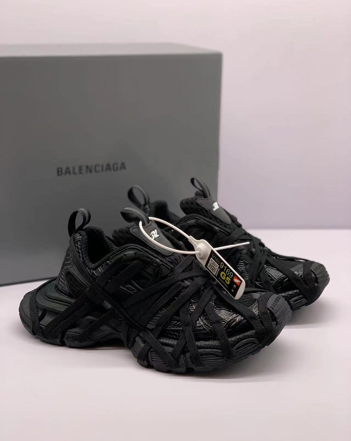 Three-quarter view of black sneakers with pull tabs, padded collars, and a Balenciaga-branded box in the background.