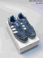 Pair of dark adidas Samba OG sneakers with white stripes displayed on an adidas shoebox.