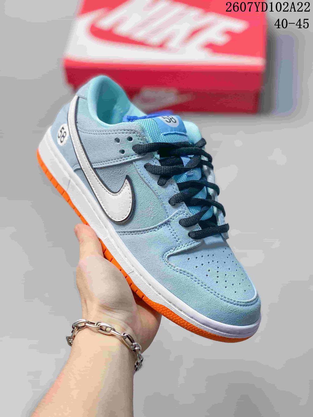 Light blue Nike SB Dunk Low Pro sneaker with a white Swoosh, dark laces and orange outsole.
