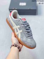Angled side view of the gray Onitsuka Tiger sneaker with cream stripes, red heel accent, and amber-colored outsole; image text shows style code 2607LY976A26 and size range 40–45.