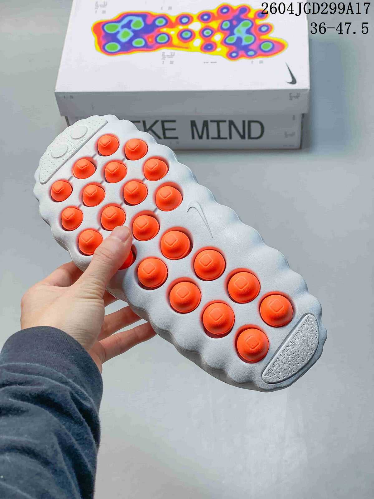 Underside view of a white Nike Mind slide showing multiple orange circular outsole elements and the textured sole.