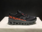 Side view highlighting the orange ON RUNNING graphic, black upper, and segmented outsole.