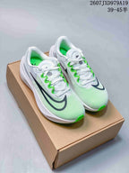 Pair of white Nike running sneakers with green accents and black side branding displayed on a shoebox.