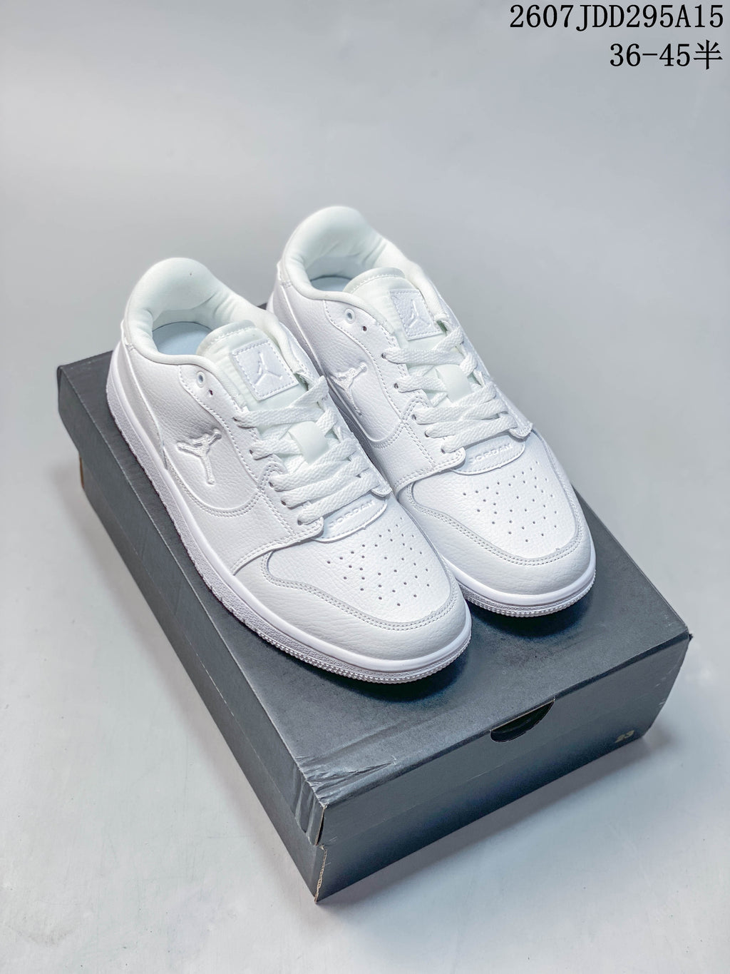 Pair of all-white Air Jordan 1 Low sneakers displayed on a black shoebox; overlay text shows style code 2607JDD295A15 and size range 36–45.