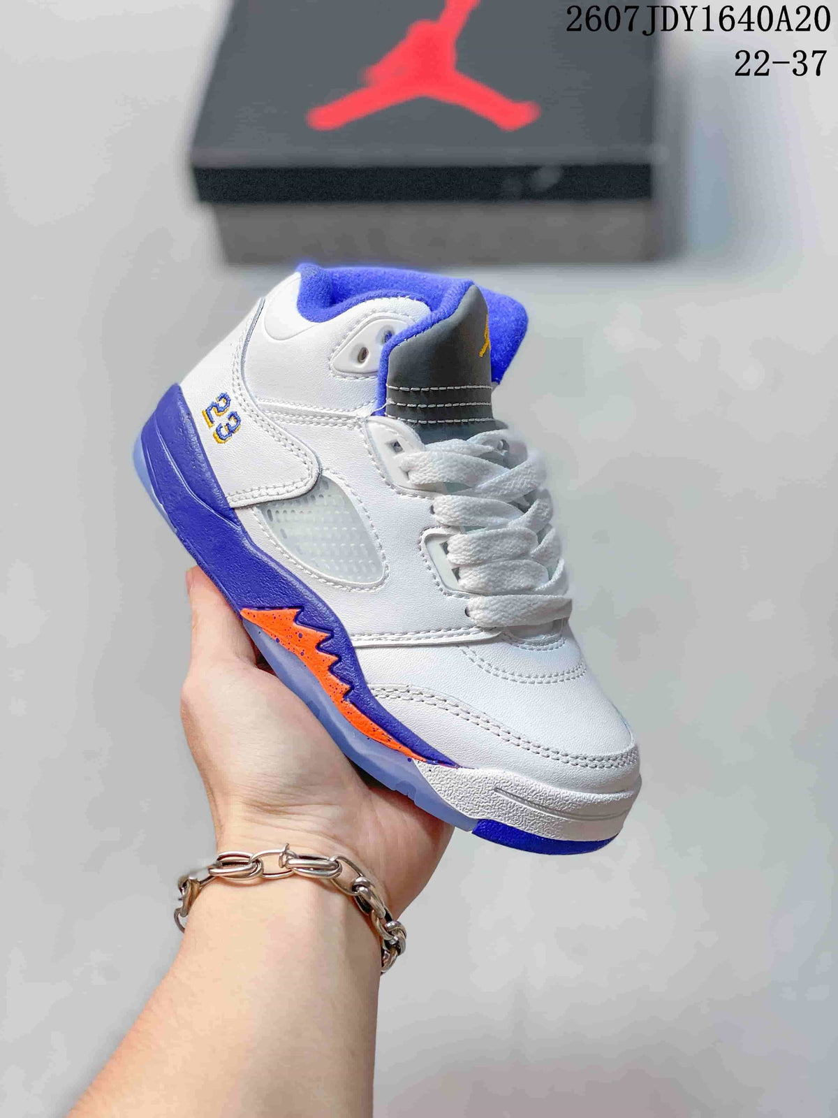 White kids' mid-top sneaker with blue and orange outsole accents and blue collar lining.